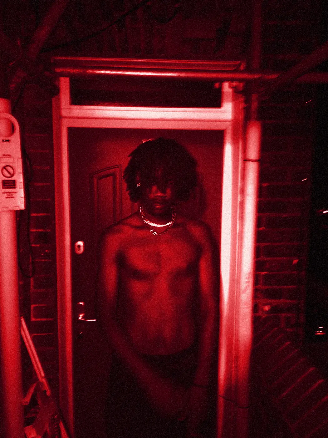 yukan shirtless in front of a red front door at night, flash-lit.