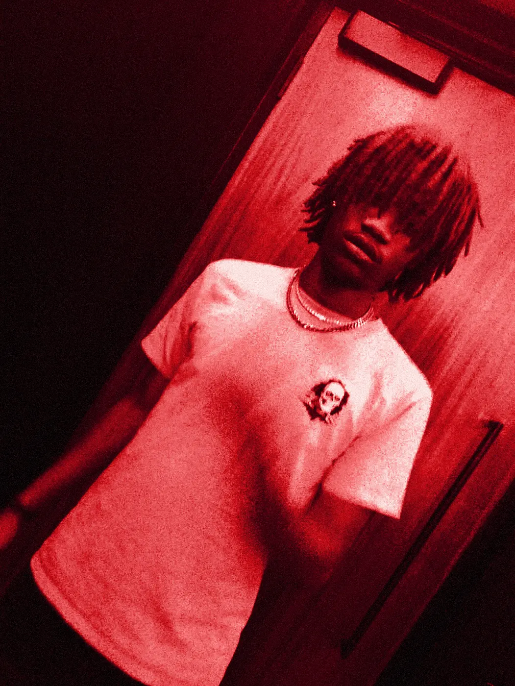 yukan leaning back in the red room, lit from below.