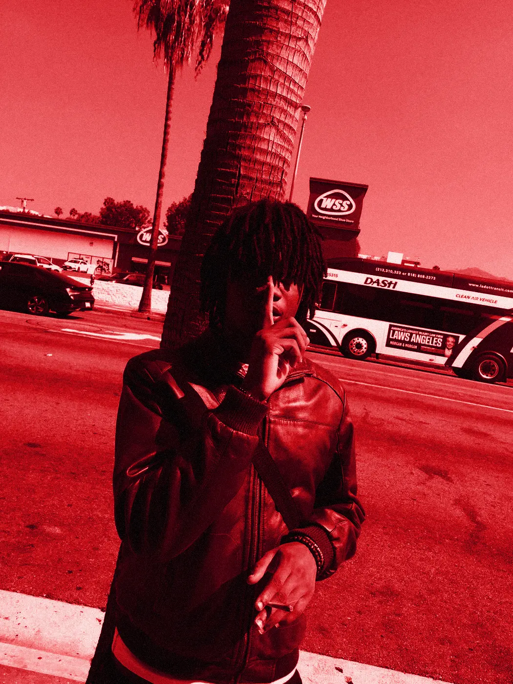 yukan in a burgundy leather jacket under a palm tree in Los Angeles, finger to his lips.