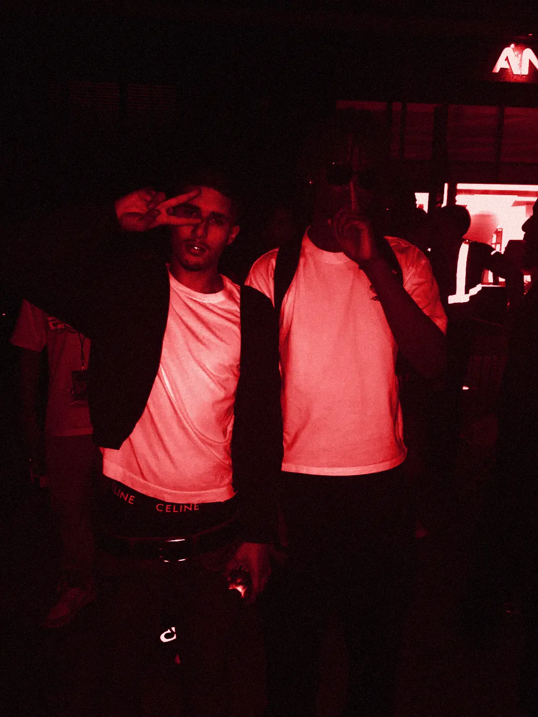 yukan and a friend in a dark venue, one throwing up a peace sign.