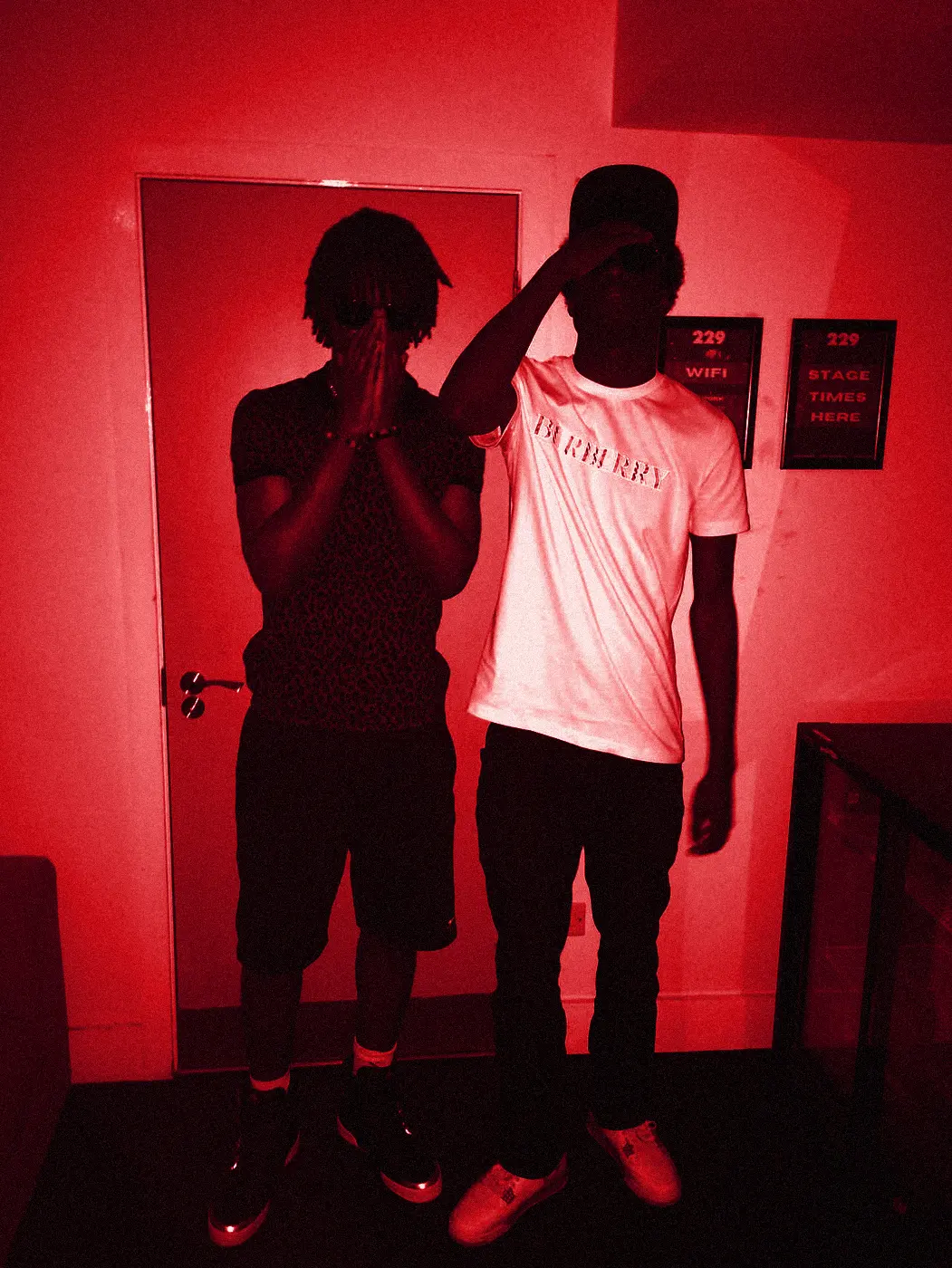 yukan and a friend in sunglasses against a white wall, one in a red patterned shirt.